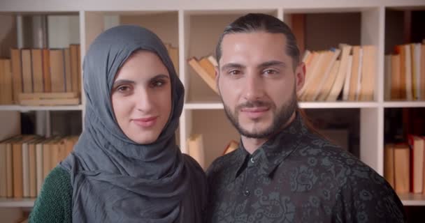 図書館大学のカメラをまっすぐ見つめている若いイスラム教徒の女性と男子学生のクローズアップ撮影 — ストック動画