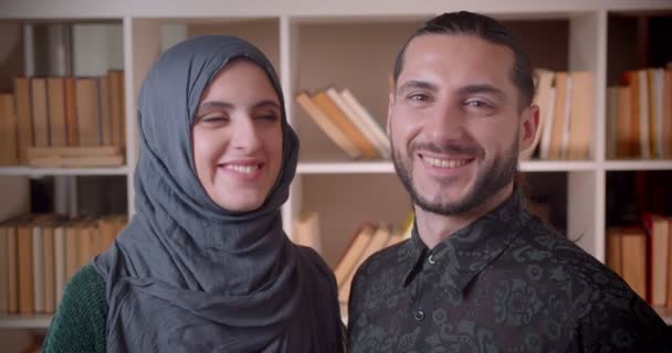 Крупним планом знімок молодих мусульманських студентів-жінки і чоловіків, які дивляться прямо на камеру і весело посміхаються в бібліотечному університеті — стокове відео