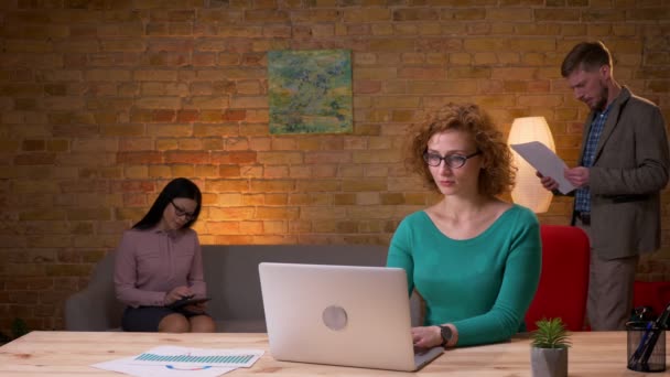 Крупним планом знімання дорослої бізнес-леді, використовуючи ноутбук, збуджується і святкується з двома жінками-колегами в приміщенні в офісі — стокове відео