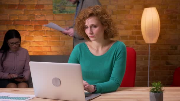 Closeup shoot of adult businesswoman typing on the laptop indoors in the office. Female and male coolleagues discussing data on the background — Stock Video