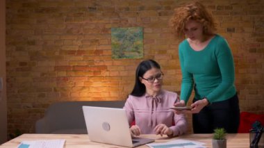 Ofiste dizüstü bilgisayar üzerinde çalışan yetişkin Asya iş kadını Closeup ateş. Ona kahve getiren erkek çalışan ve tabletteki verileri tartışan kadın çalışan