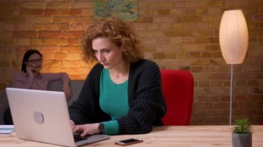 Bir telefon görüşmesi olan dizüstü bilgisayar üzerinde çalışan genç iş kadını Closeup ateş ve ofiste memnuniyeti ile rahat rahatlatıcı. Arka planda cep telefonu arayan kadın çalışan