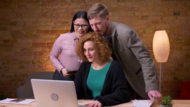 Ofiste ki dizüstü bilgisayarı kullanarak yetişkin beyaz iş kadınının yakın çekim çekimi. Bilgisayarda görüntülü arama yapıyor ve eğleniyor üç çalışan
