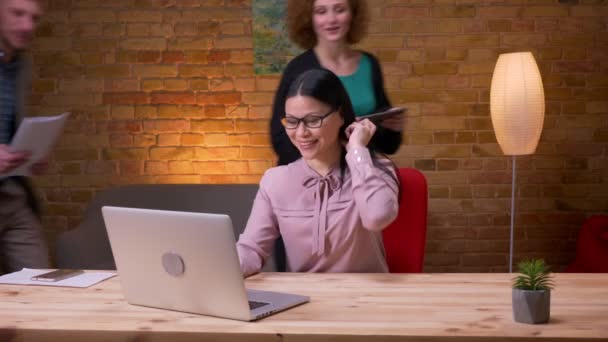 Närbild shoot av vuxna asiatiska affärskvinna med hjälp av den bärbara datorn inomhus på kontoret. Tre anställda som har ett videosamtal på datorn och ha kul — Stockvideo
