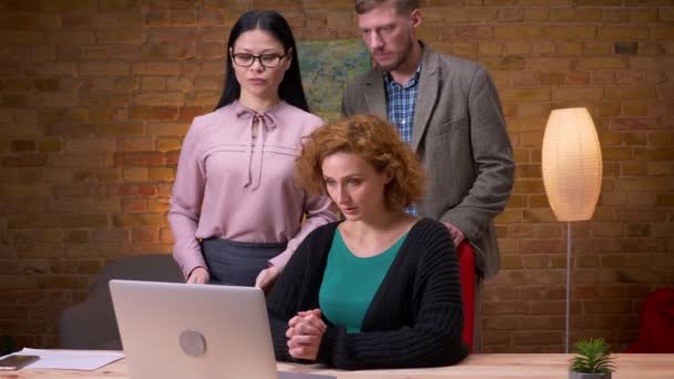 Close-up shoot van volwassen blanke zakenvrouw die de laptop binnenshuis op kantoor gebruikt. Drie werknemers met een videogesprek met een baas op de computer — Stockvideo