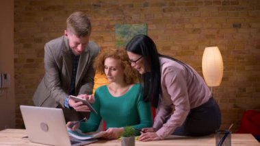 Dizüstü tablet ve işyerinde iç mekanlarda mutlu bir şekilde gülen grafikleri kullanarak verileri tartışan üç ofis çalışanının yakın çekim çekimi