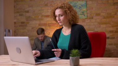 Ofiste ki dizüstü bilgisayar üzerinde çalışan yetişkin beyaz iş kadınının yakın çekim çekimi. İşadamı kağıtlarını kanepede otururken ve arka planda tableti kullanarak kullanırken