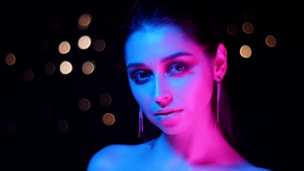 Close-up shoot van jonge prachtige Kaukasische vrouw met neon licht en bokeh achtergrond poseren in de voorkant van de camera — Stockvideo