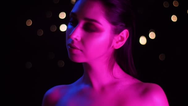 Nahaufnahme einer jungen atemberaubenden kaukasischen Frau mit rosa Neonlicht und Bokeh-Hintergrund, die vor der Kamera posiert — Stockvideo