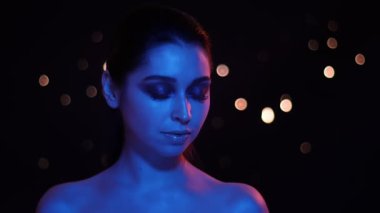 Kamera önünde poz mavi ve kırmızı neon ışık ve bokeh arka plan ile çarpıcı glitter makyaj ile genç güzel kafkas kadın Closeup ateş