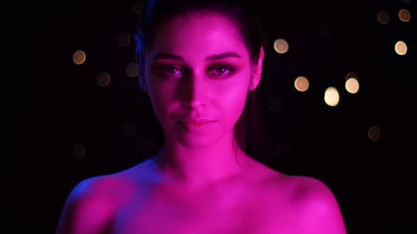 Primer plano de la joven impresionante hembra caucásica con luz de neón rosa y fondo bokeh seductora posando delante de la cámara — Vídeo de stock