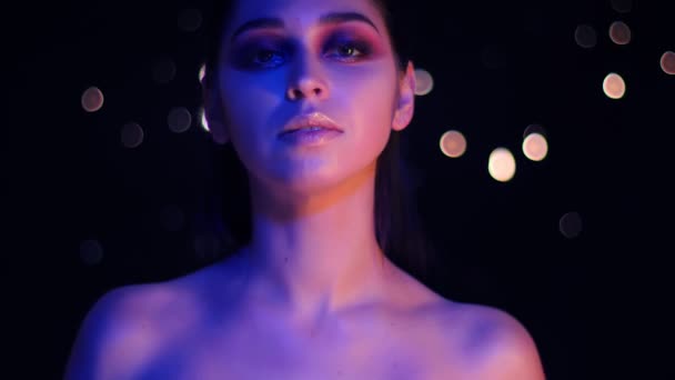 Nahaufnahme einer jungen atemberaubenden kaukasischen Frau mit lila Neonlicht und Bokeh-Hintergrund, die vor der Kamera posiert — Stockvideo