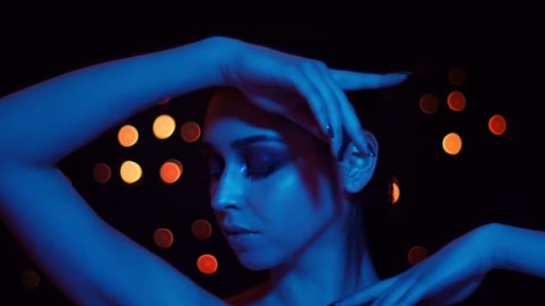 Primo piano di ripresa di giovane bella femmina caucasica con trucco mozzafiato con luce blu al neon e luci bokeh sullo sfondo in posa davanti alla fotocamera — Video Stock