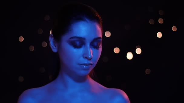 Nahaufnahme einer jungen hübschen kaukasischen Frau mit atemberaubendem Glitzer-Make-up mit blauem und rotem Neonlicht und Bokeh-Hintergrund, die vor der Kamera posiert — Stockvideo