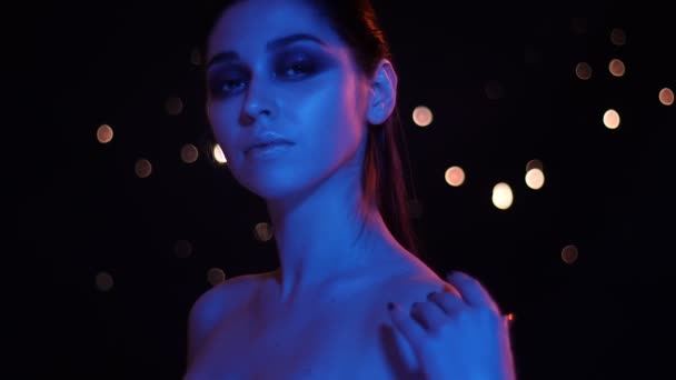 Kamera önünde poz mavi ve kırmızı neon ışık ve bokeh arka plan ile çıplak omuzlu genç güzel beyaz kadın Closeup ateş — Stok video