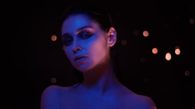 Kameraya bakarak mor neon ışık ve bokeh arka plan ile glitter makyaj ile güzel kadın Closeup ateş