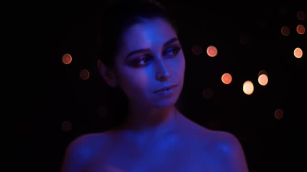 카메라 앞에서 포즈를 취하는 파란색과 빨간색 네온 빛과 보케 배경으로 반짝이는 메이크업으로 젊은 아름다운 백인 여성의 클로즈업 촬영 — 비디오