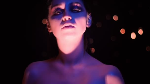Closeup, fotr mladé bělošské ženy s úžasným třpytím na pozadí s růžovým a žlutým světlem a bokeh na kameře — Stock video