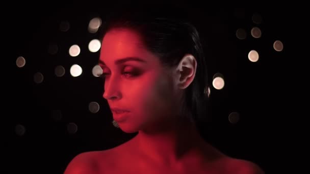 Närbild shoot av Pretty förförisk hona med fantastisk makeup med rött neonljus och bokeh bakgrund poserar framför kameran — Stockvideo