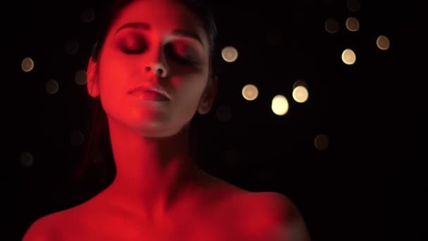 Close-up shoot van vrij verleidelijke vrouw met mooie make-up met rode neon licht en bokeh achtergrond poseren in de voorkant van de camera — Stockvideo