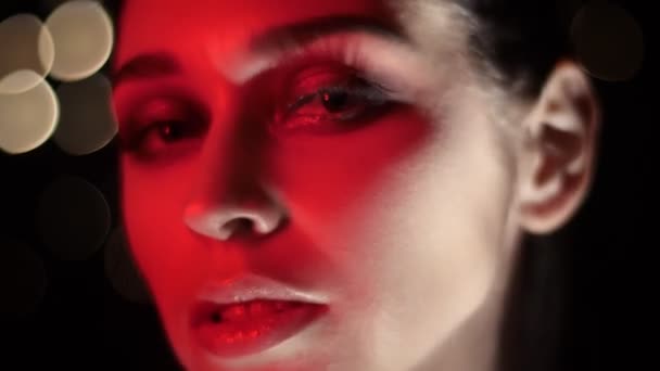 Closeup lő csinos női arc lenyűgöző smink vörös Neonfény és bokeh háttér nézi kamera — Stock videók
