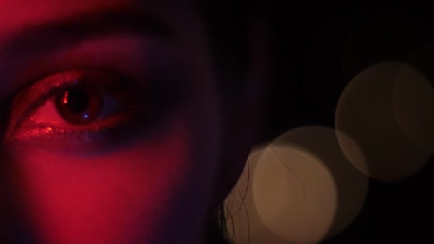 Closeup meia-face atirar de olhos femininos bonitos com maquiagem sedutora com luz de néon vermelho e fundo bokeh na boate — Vídeo de Stock