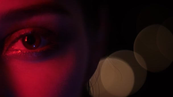 Sesión de media cara de ojos femeninos bonitos con maquillaje seductor con luz de neón roja y fondo bokeh en el club nocturno — Vídeo de stock