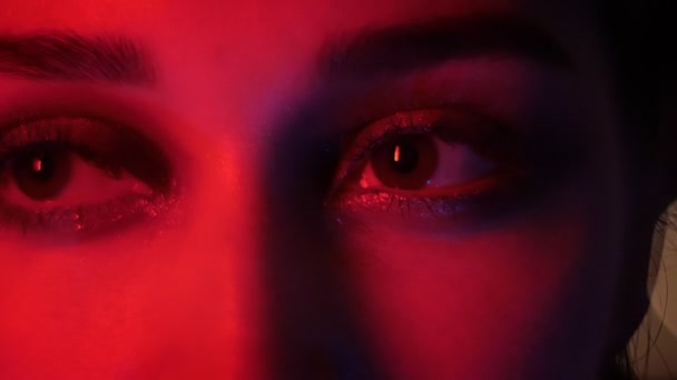 Closeup shoot of pretty female eyes with seductive vogue makeup with red neon light and bokeh background looking at camera at nightclub — Stock Video