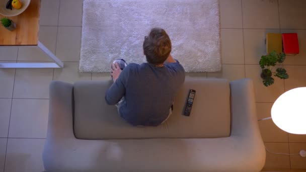 Tv'de spor izleyen genç rahat giyimli erkek Closeup üst ateş rahat evde mutlu kapalı almak kanepede oturan — Stok video
