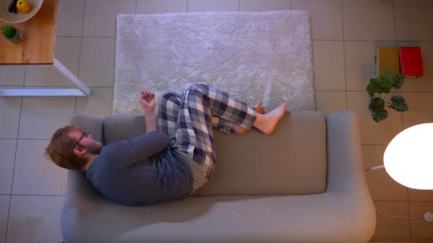 Närbild topp shoot av unga nonchalant klädd manlig tittar på TV liggande på soffan är deprimerad och ledsen inomhus på Cozy Home — Stockvideo