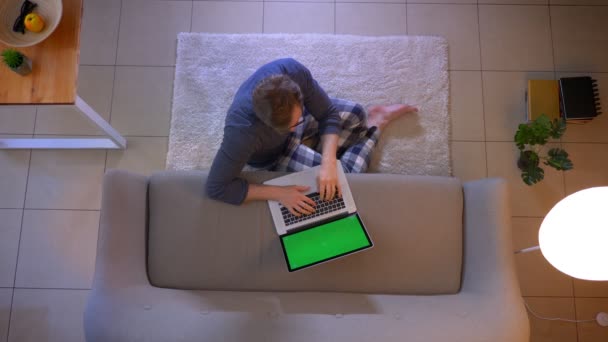 Close-up top shoot de jovens casualmente vestido masculino digitando no laptop sentado no chão dentro de casa aconchegante — Vídeo de Stock