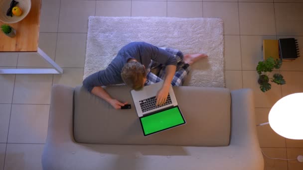 Hlavní střílečka mladého, nedbale oblečeného mužského nakupování on-line s kreditní kartou na přenosném počítači, která sedí na podlaze doma v útulném domě — Stock video