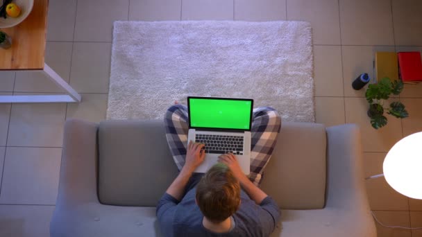 Nahaufnahme Top-Shooting junger männlicher Studenten online mit dem Laptop mit grünem Bildschirm, während sie zu Hause auf dem Sofa sitzen — Stockvideo