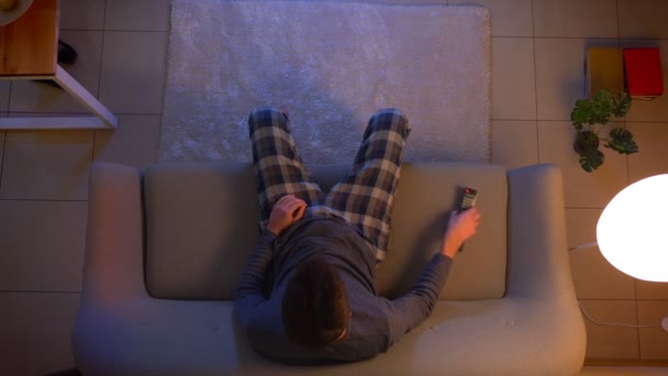 Primo piano top shot di giovane maschio guardando una partita di calcio in TV seduto sul divano ottenere sconvolto e frustrato al chiuso a casa accogliente con le luci spente la sera — Video Stock