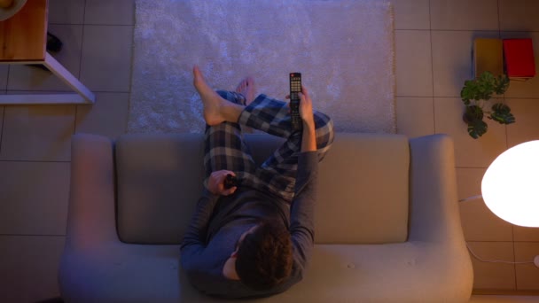 Nahaufnahme Top-Shooting junger Männer, die Sport im Fernsehen verfolgen, auf der Couch sitzen und mit Fernbedienung zu Hause mit ausgeschaltetem Licht Bier trinken — Stockvideo