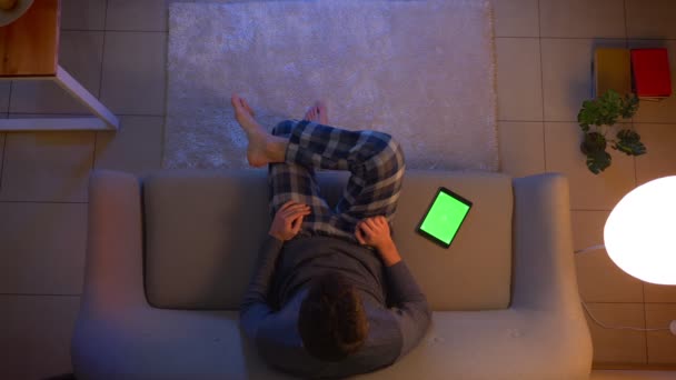 Крупный план верхней съемки молодых мужчин смотреть телевизор и с помощью приложения на планшете с зеленым экраном в качестве пульта дистанционного управления, чтобы выключить в помещении в уютном доме в вечернее время — стоковое видео