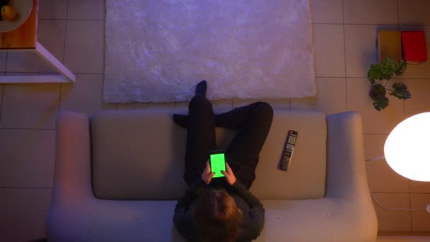 Nahaufnahme Top-Shooting von jungen hübschen weiblichen SMS am Telefon, während Fernsehen und sitzen auf der Couch drinnen zu Hause gemütlich am Abend — Stockvideo