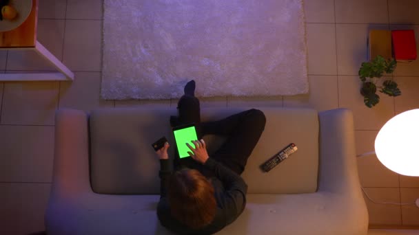 Nahaufnahme Top-Shooting von jungen hübschen weiblichen Online-Shopping auf dem Tablet mit grünem Bildschirm vor dem Fernseher und sitzen auf der Couch drinnen zu Hause gemütlich am Abend — Stockvideo