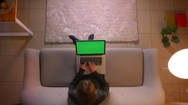 Closeup top shoot of young pretty female typing on the laptop with green screen while sitting on the couch indoors at cozy home — Stock Video