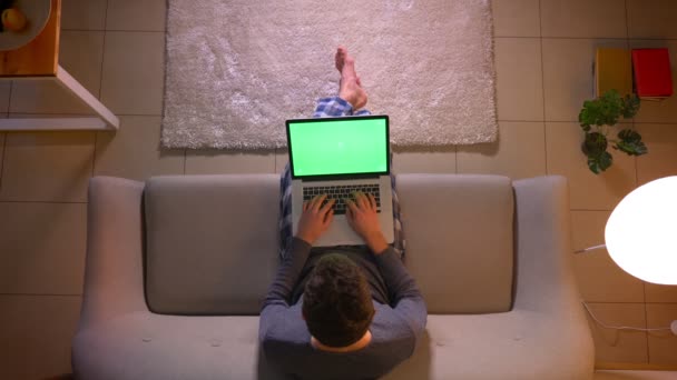 Nahaufnahme Top-Shooting junger Mann Nachrichten auf dem Laptop mit grünem Bildschirm, während er auf der Couch zu Hause gemütlich sitzen — Stockvideo