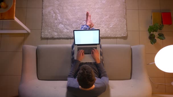 Nahaufnahme Top-Shooting des jungen Geschäftsmannes, der auf dem Laptop mit grünem Bildschirm arbeitet, während er zu Hause auf der Couch sitzt — Stockvideo