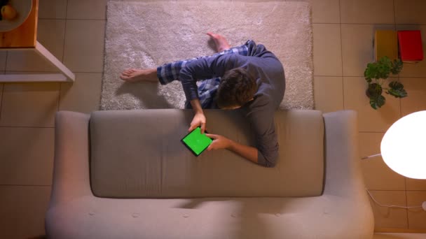 Gros plan tige supérieure de jeune homme textos sur la tablette avec écran vert tout en étant assis sur le sol à l'intérieur à la maison confortable — Video