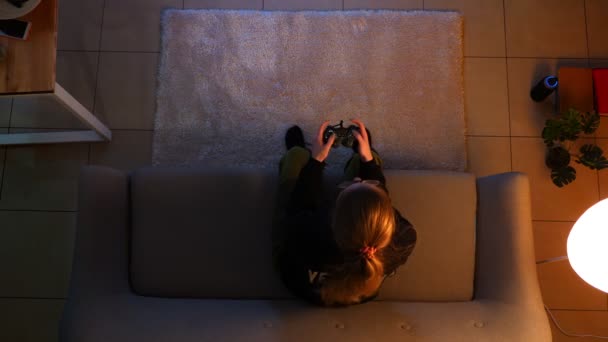 Primo piano top shoot di graziosi videogiochi femminili sulla xbox utilizzando la console di gioco mentre si siede sul divano al chiuso in un accogliente appartamento con luci spente — Video Stock