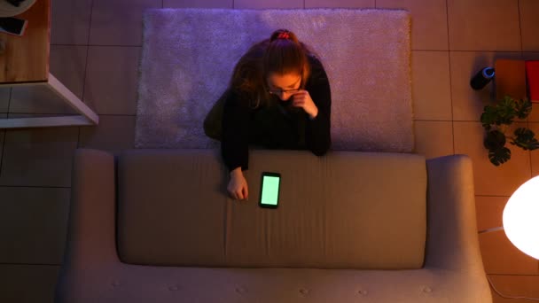 Gros plan top shoot de jolie adolescente regarder la télévision en utilisant le téléphone avec écran vert tout en étant assis sur le tapis à l'intérieur dans un appartement confortable — Video