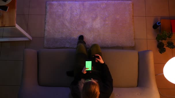 Closeup top shoot of pretty female teenager watching TV using the phone shopping online while sitting on the couch indoors in a cozy apartment — Stock Video