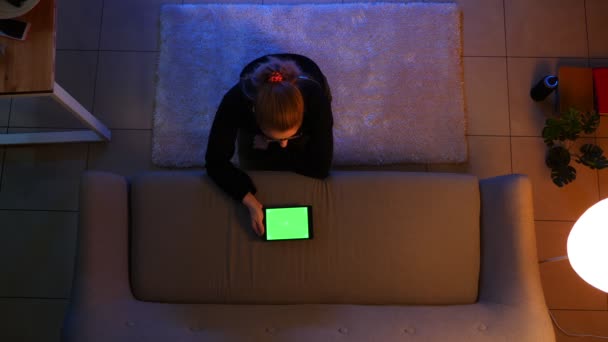 Closeup top shoot of pretty female using the tablet with green screen and messaging while sitting on the carpet indoors in a cozy apartment — Stock Video