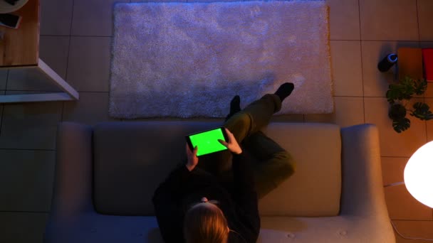 Крупним планом зйомка красивої жінки, використовуючи планшет з зеленим екраном і граючи в відеоігри, сидячи на дивані в приміщенні в затишній квартирі — стокове відео
