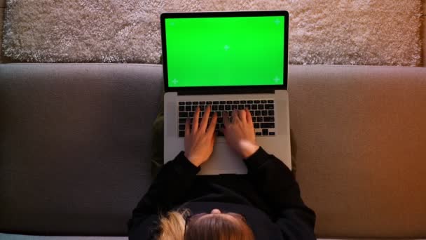 Closeup top shoot of pretty female using the laptop with green chroma screen and networking while sitting on the sofa indoors in a cozy apartment — Stock Video