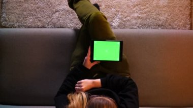 Bir süre rahat bir dairede kanepede oturan yeşil ekran ile tablet kullanarak güzel kız Closeup üst ateş