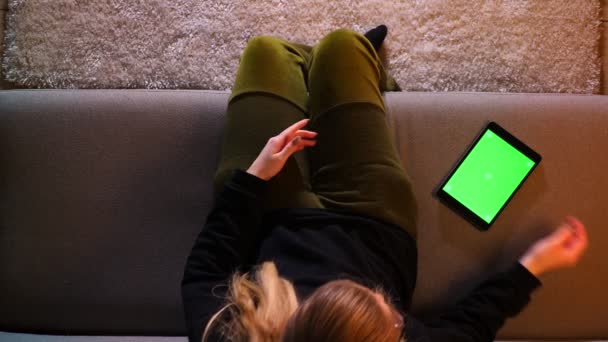 Primer plano brote de mensajería chica bonita en la tableta con pantalla verde emocionándose mientras se sienta en el sofá en un acogedor apartamento — Vídeos de Stock